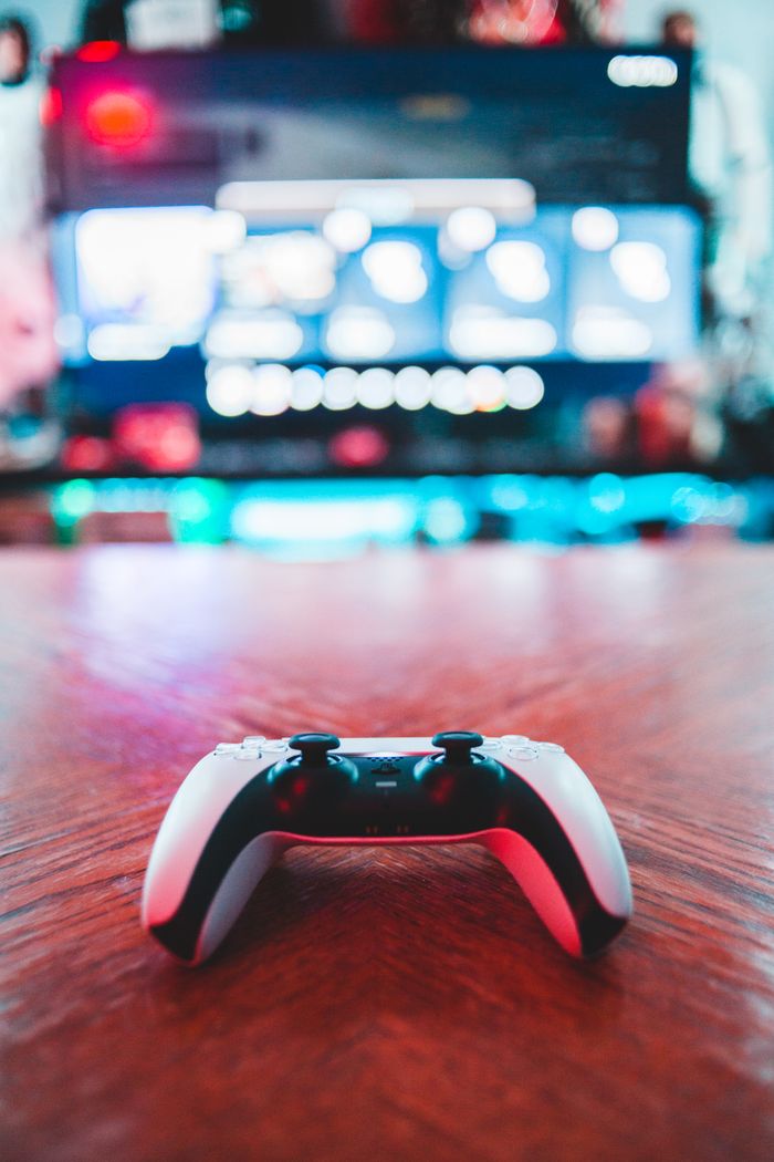 services-01 A close-up of a gaming controller on a wooden table with vibrant screen in the background.